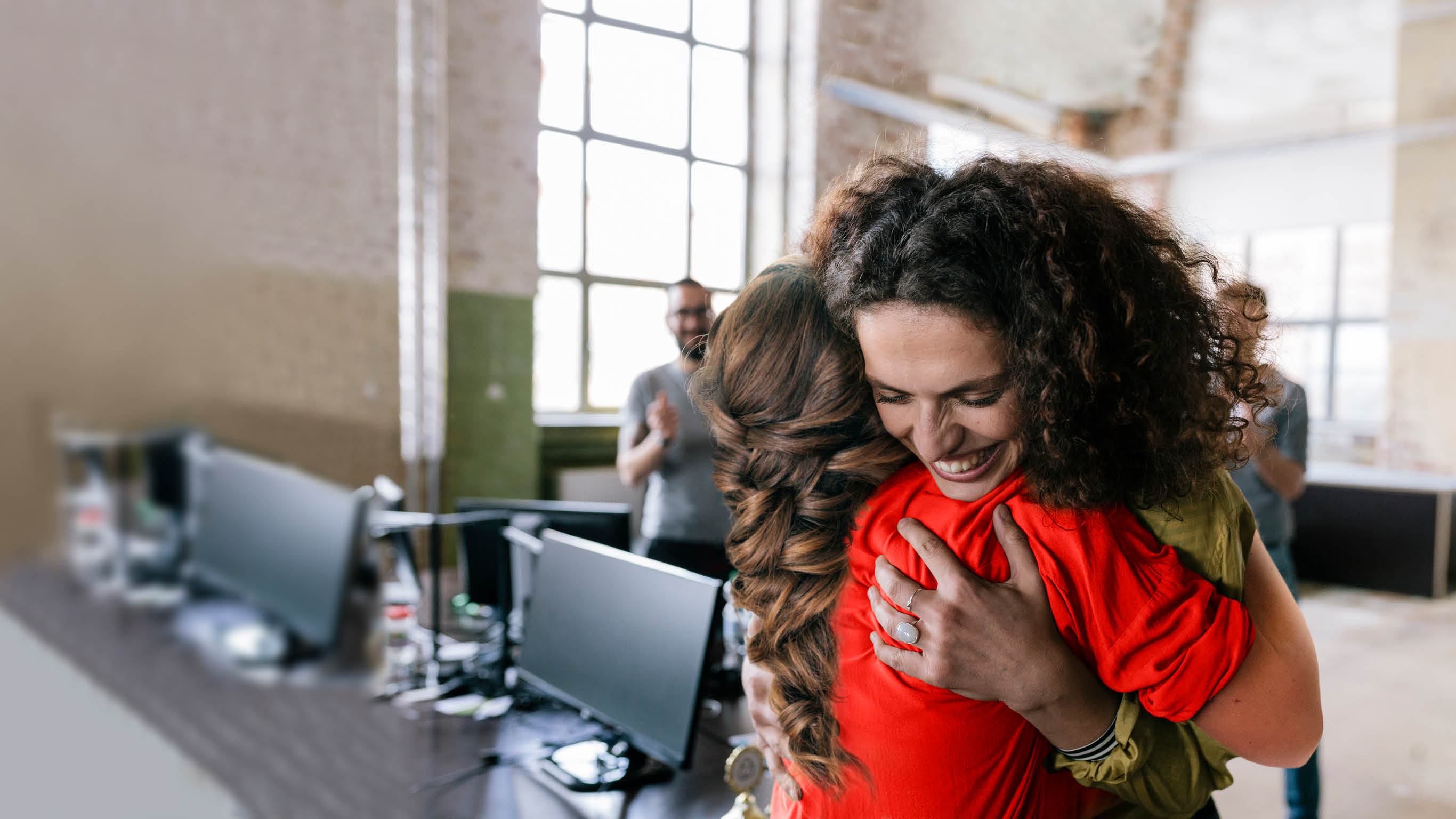 People in a startup business space celebrating a co-worker  Woman is being hugged by one of her co-worker 