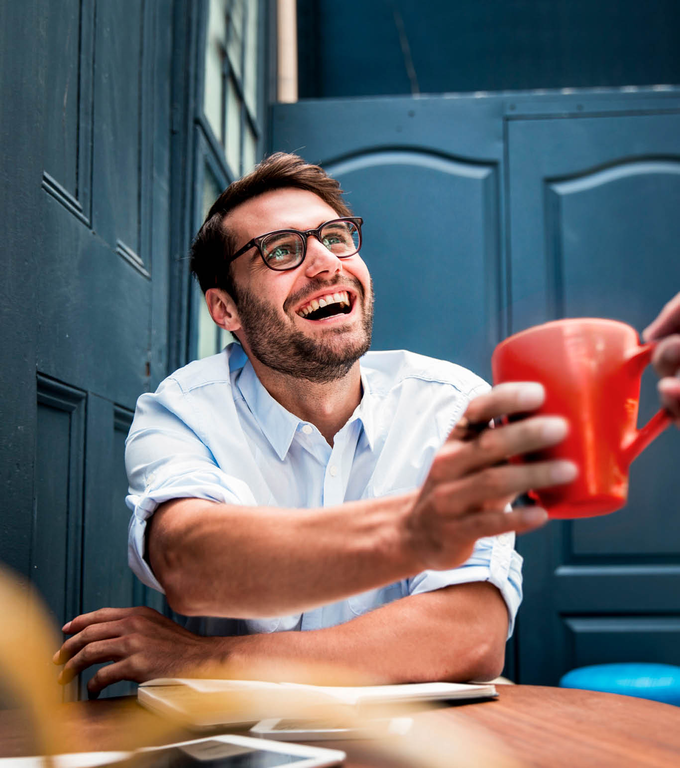 A photo of cropped hand giving coffee mug to cheerful businessman in office  Happy male professional sitting at desk  Handsome executive is wearing eyeglasses and shirt at workplace 