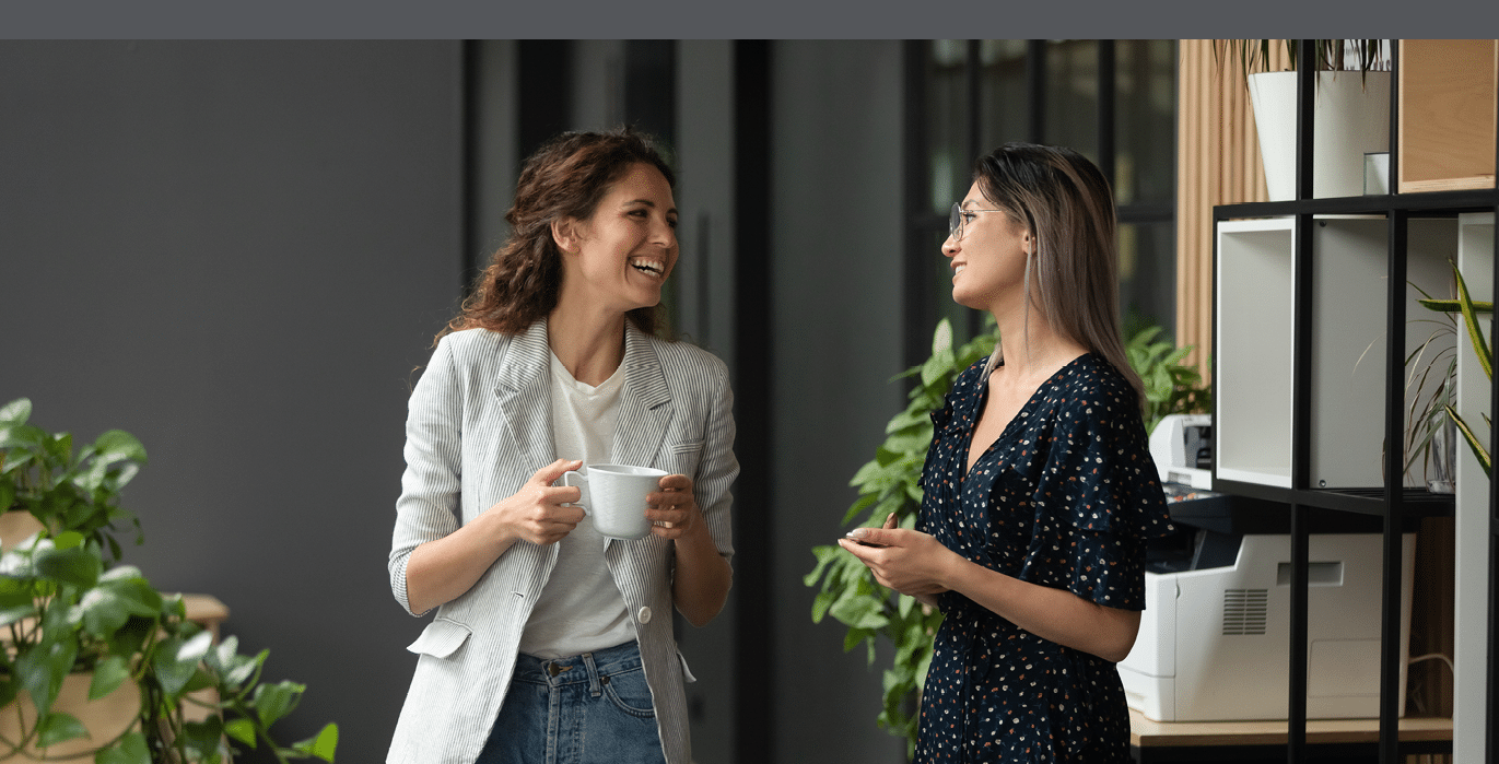 Asian and Caucasian ethnicity women colleagues met in office hall chatting enjoy friendly warm conversation, multi-ethnic mates having informal talk drink tea or coffee take break distracted from work